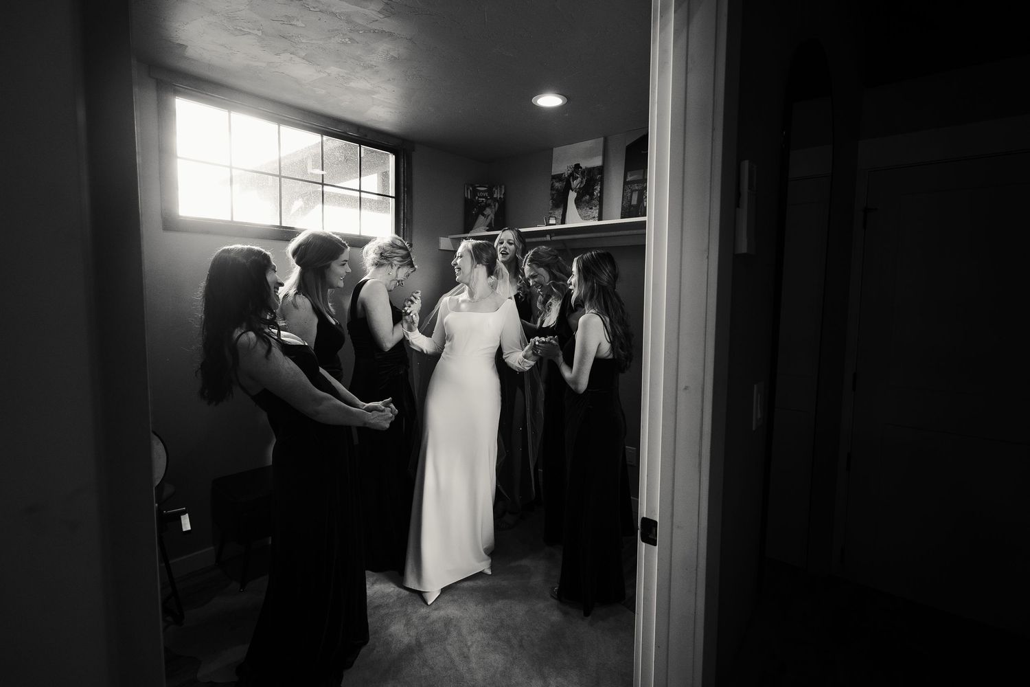 Black and white photo of bridesmaids helping a bride get ready in a small room before the wedding ceremony.
