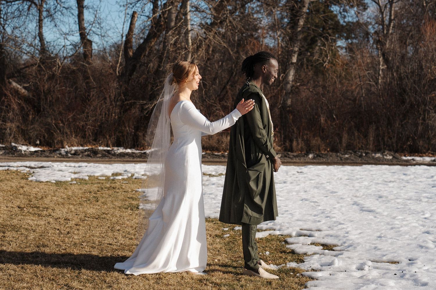 A romantic winter scene in a snowy woodlands setting shows two people in formal attire standing together.
