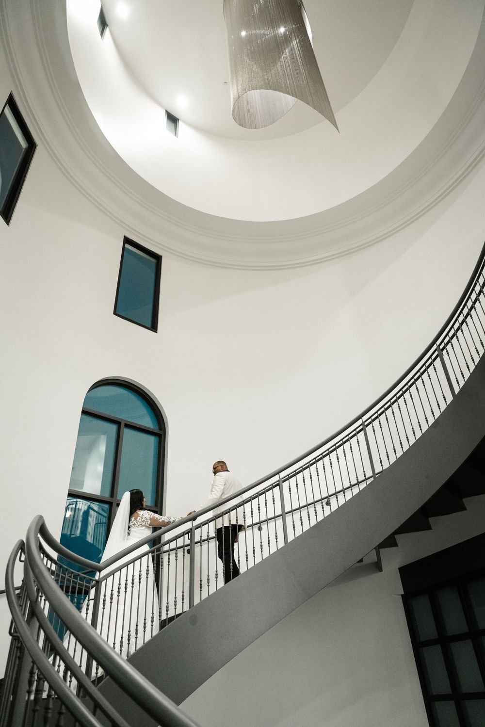 Interior architectural photo of a curved white staircase with black railings and turquoise windows in a circular space.