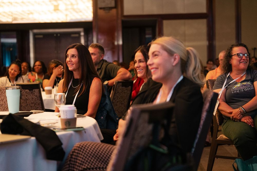 Audience members smile and engage while seated during an indoor presentation or conference event.