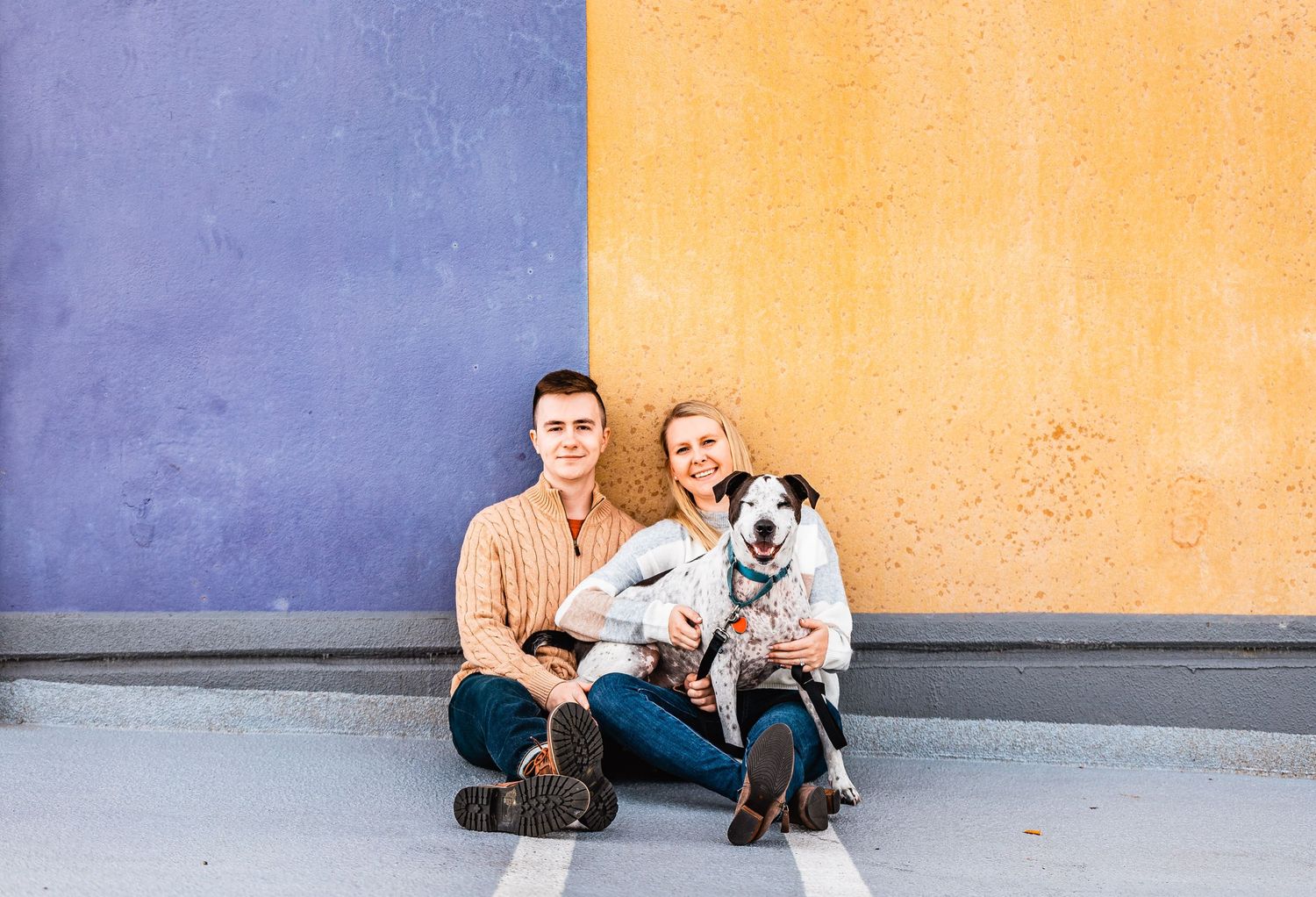 Two people sitting against colorful purple and orange wall with their spotted Dalmatian dog.