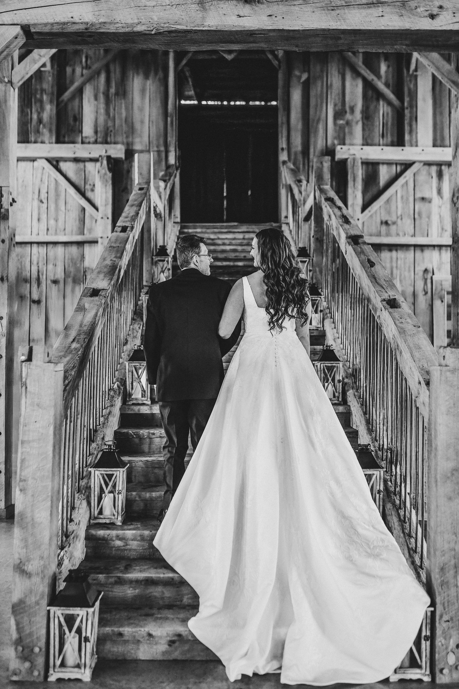 a gorgeous black and white photo of the bride and her father walking up the stairs at their rustic wedding venue