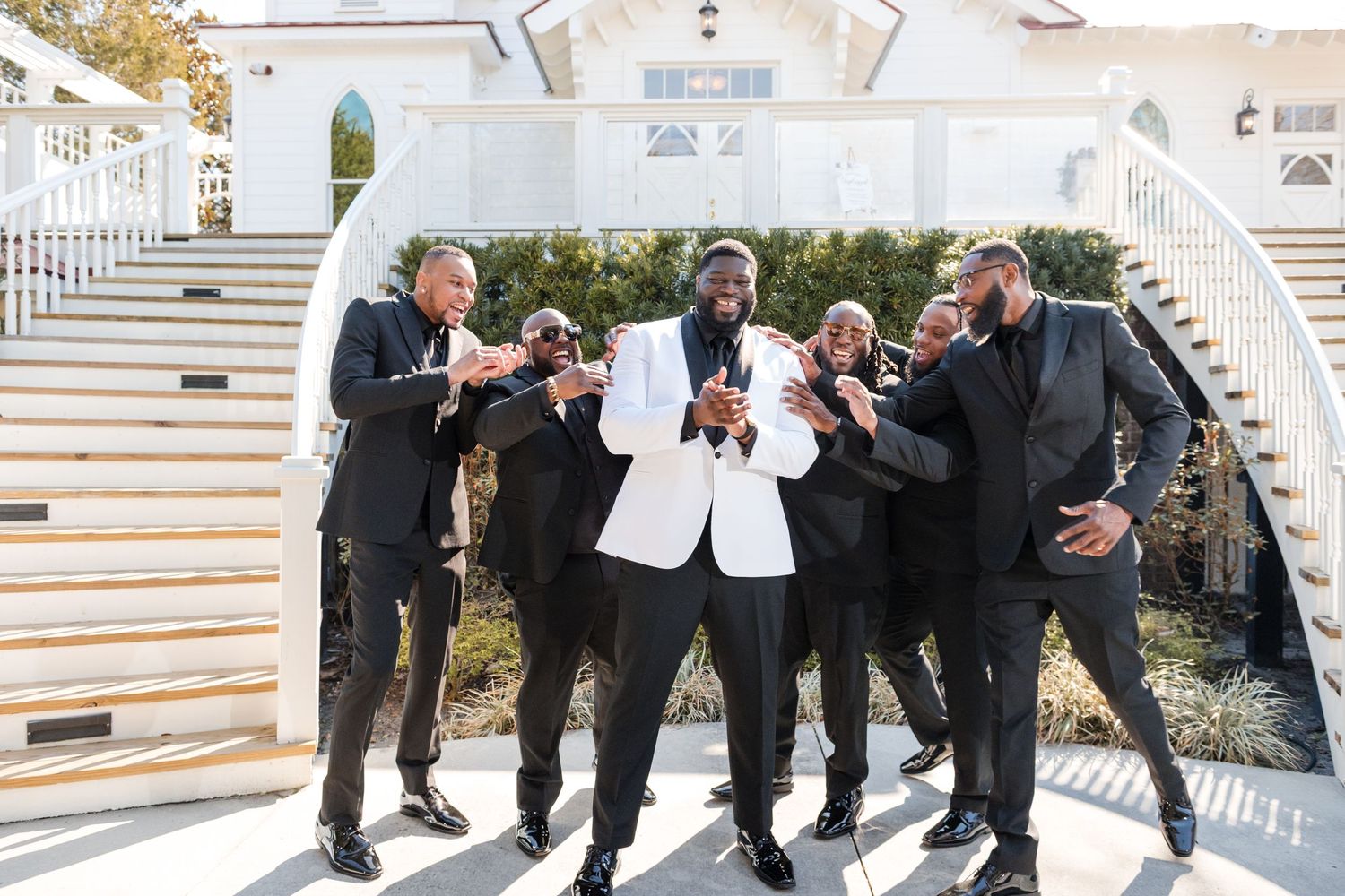 Groomsmen in formal attire share a lighthearted moment while posing on outdoor stairs.