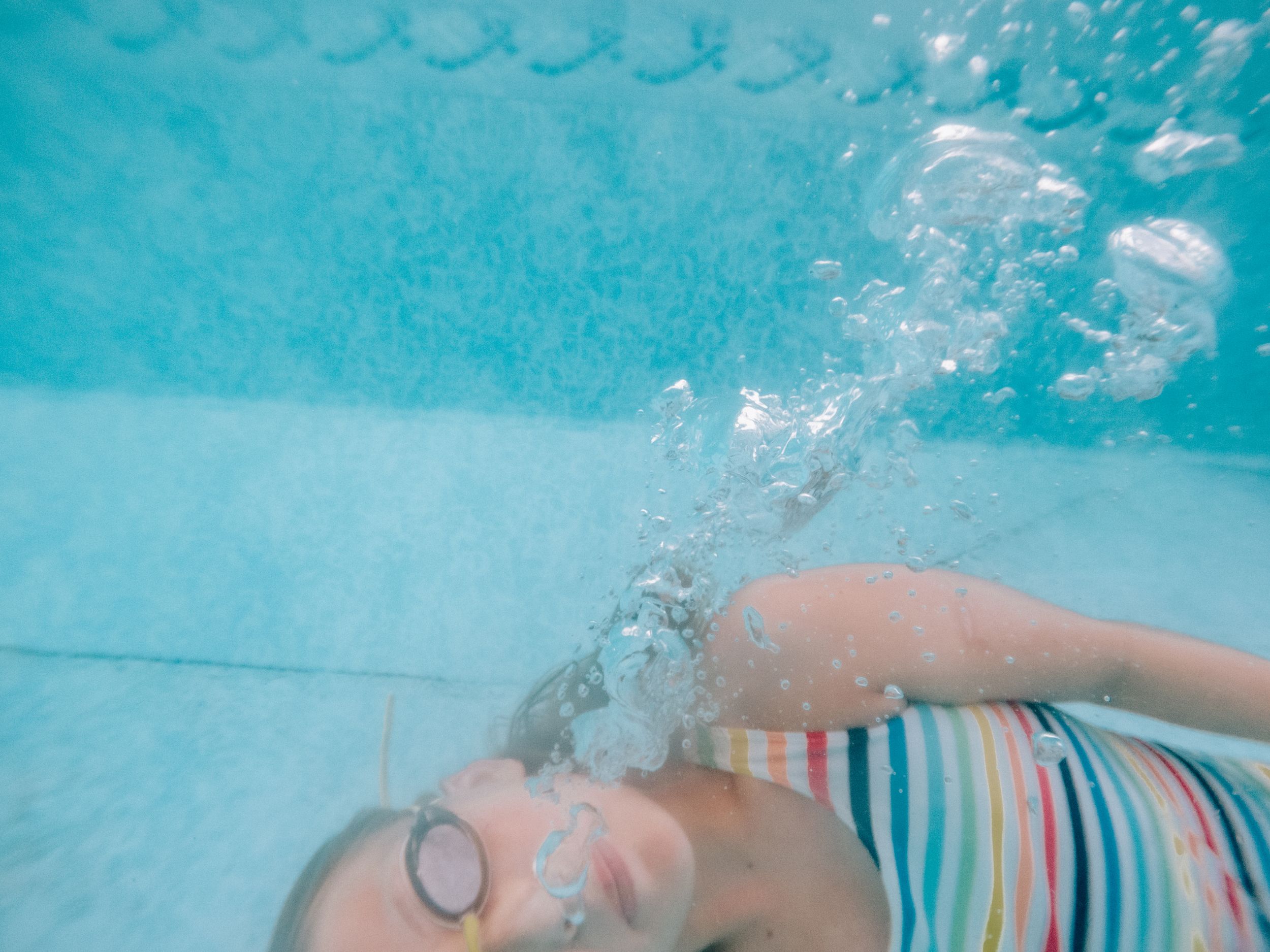 A swimmer in a blue swimsuit glides underwater against a turquoise backdrop of clear tropical waters. virginia beach photographer family