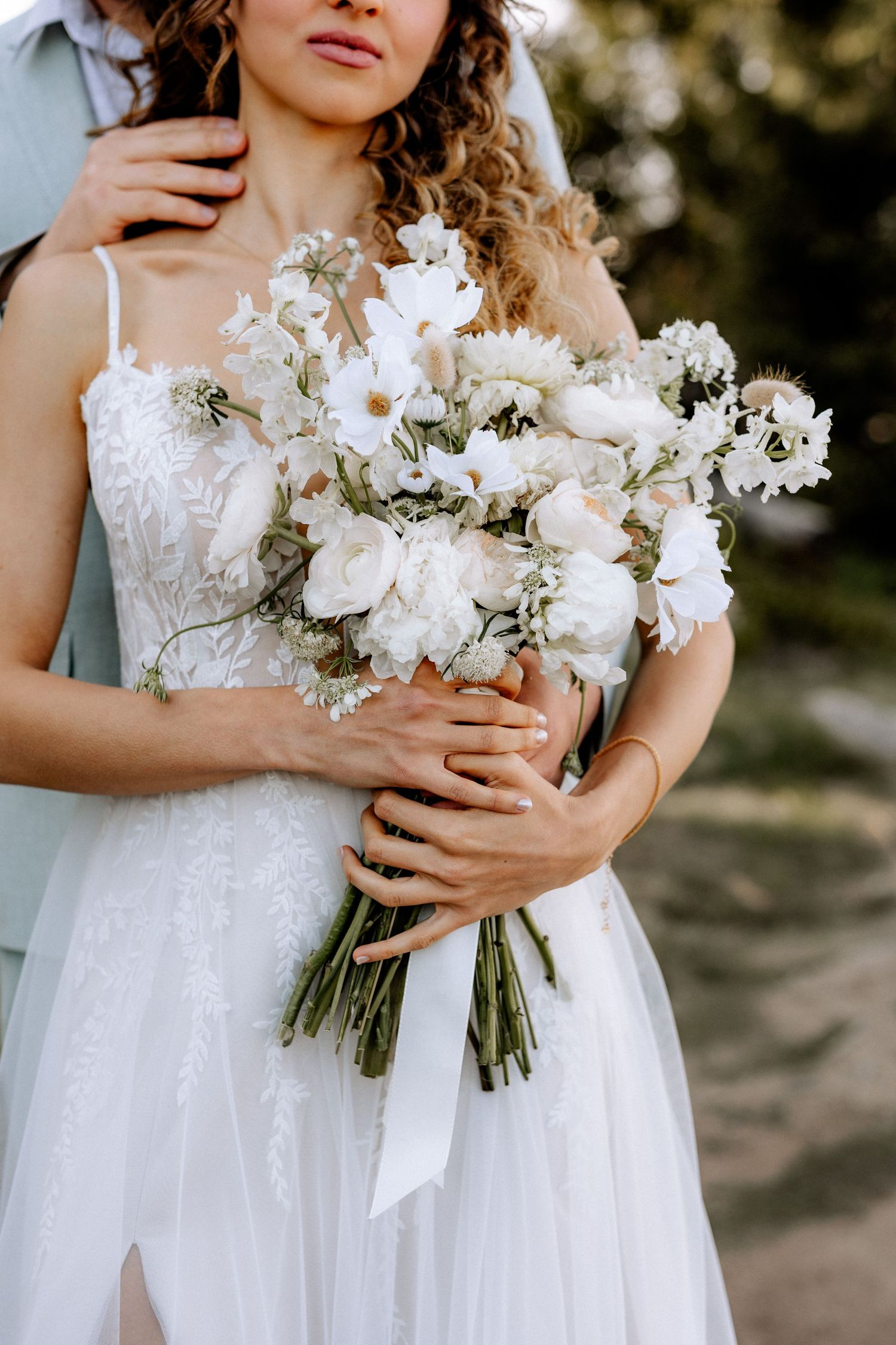 Close-up of an elegant white bridal bouquet featuring roses and delicate flowers wrapped with ribbon.