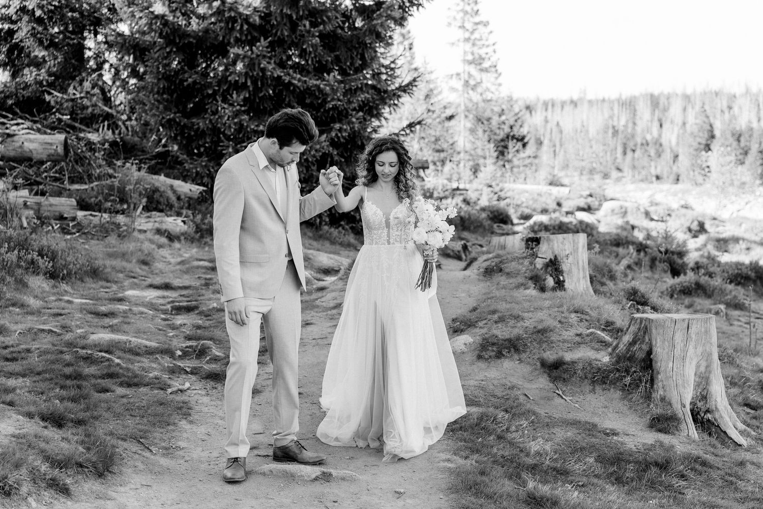 A romantic black and white outdoor wedding photo shows a couple walking together on a scenic mountain path.