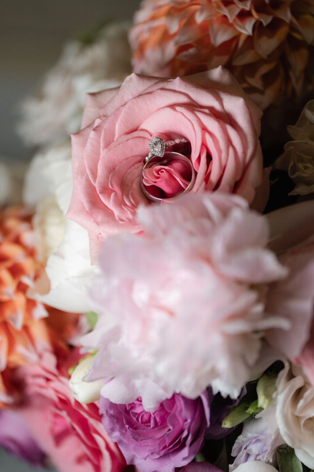 Close-up of a diamond engagement ring nestled in a pink rose surrounded by a pastel floral bouquet.