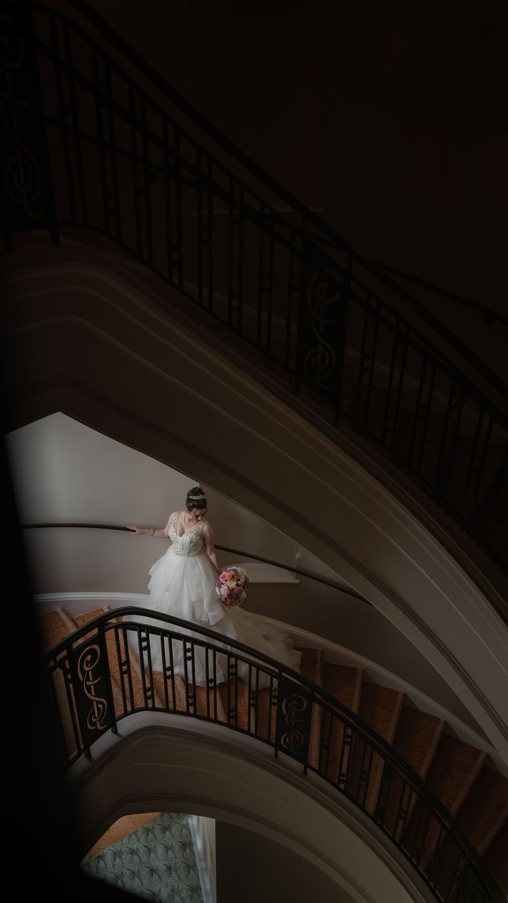 A curving grand staircase with ornate iron railings in a dimly lit elegant interior setting. Wedding in Charleston at the Galliard Cente