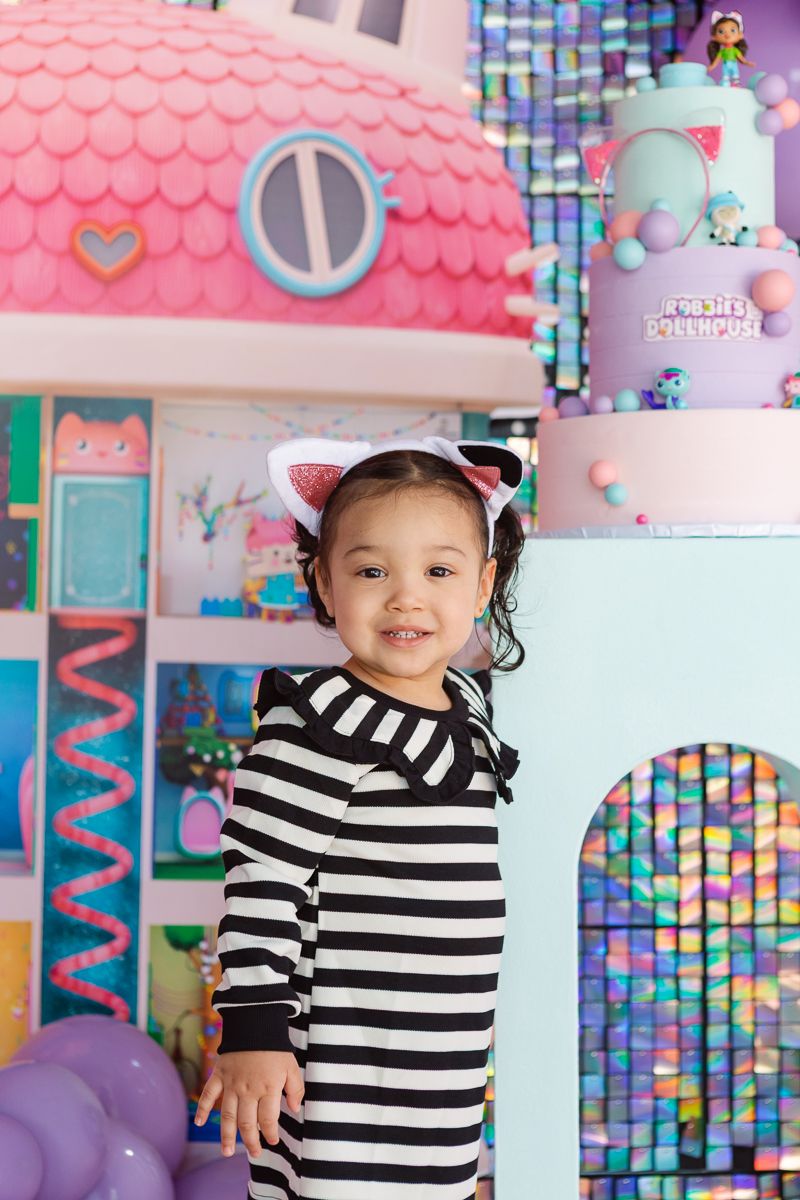 Birthday girl smiles next to Dollhouse-themed decorations at her NYC home celebration by NYC Birthday Party Photographer Paula Brearley