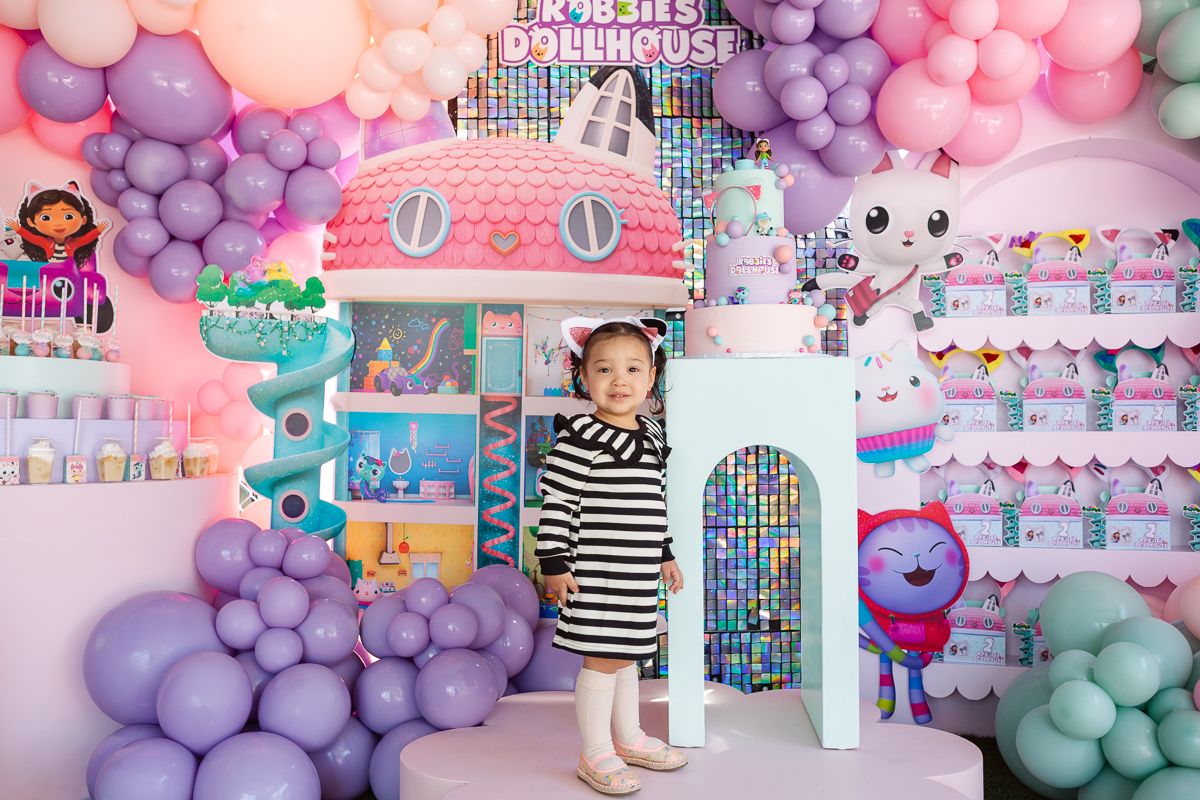 Birthday girl smiles in front of a vibrant Gaby’s Dollhouse party setup, captured by NYC family photographer Paula Brearley