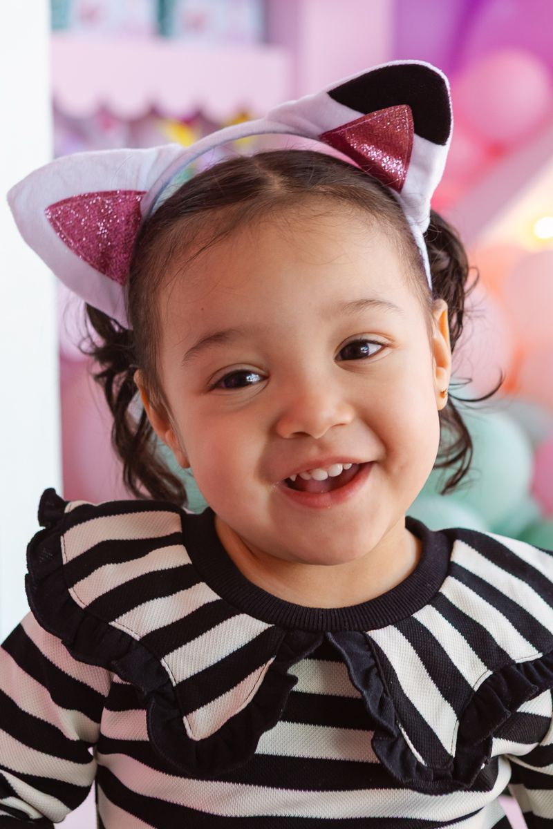 Excited birthday girl stands in front of a beautifully styled Gaby’s Dollhouse backdrop, showcasing themed decorations