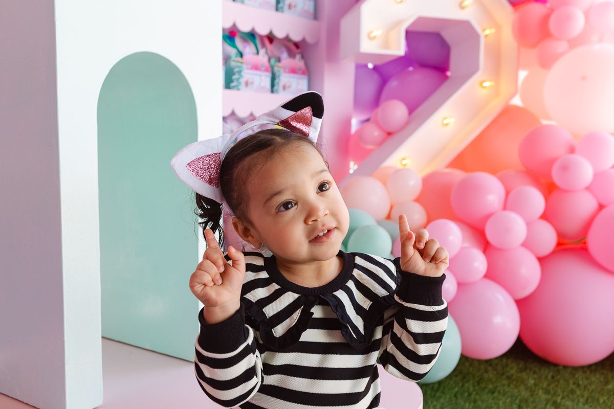 Birthday girl proudly holds up two fingers in front of her Gaby’s Dollhouse-themed party decor, celebrating her second birthday in NYC