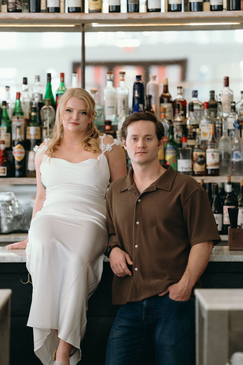 A couple poses at a well-stocked bar with extensive liquor selection.