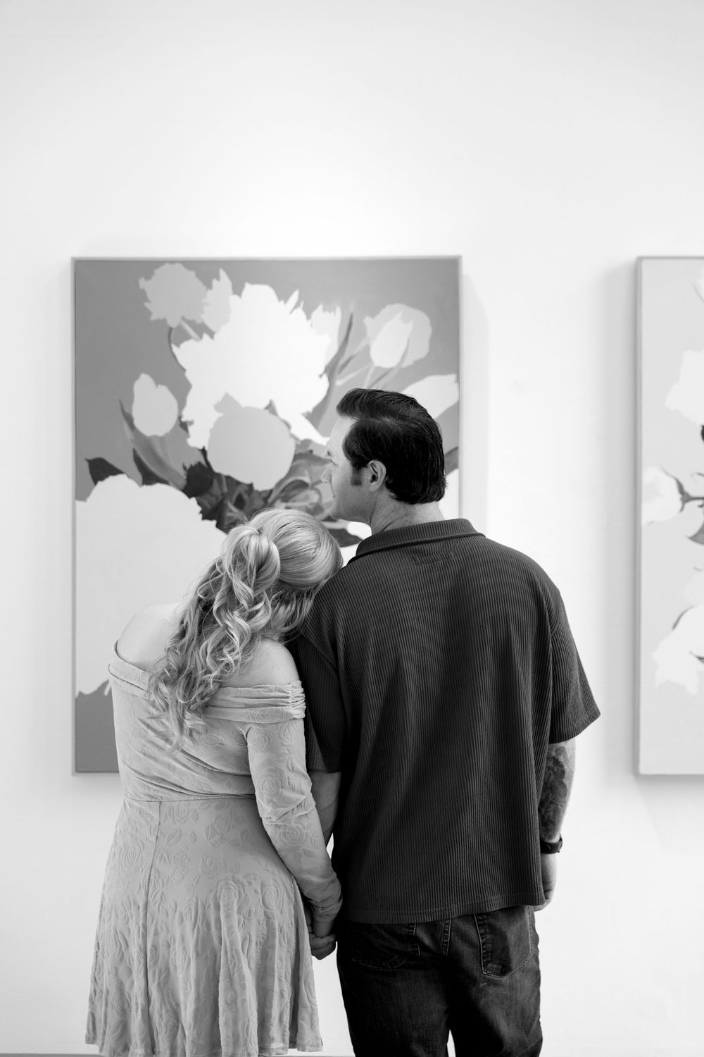 A couple views abstract floral artwork in a gallery setting.