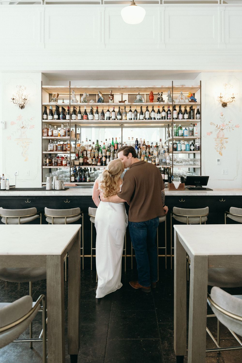 A romantic moment at an elegant bar with leather stools and shelves of liquor bottles.