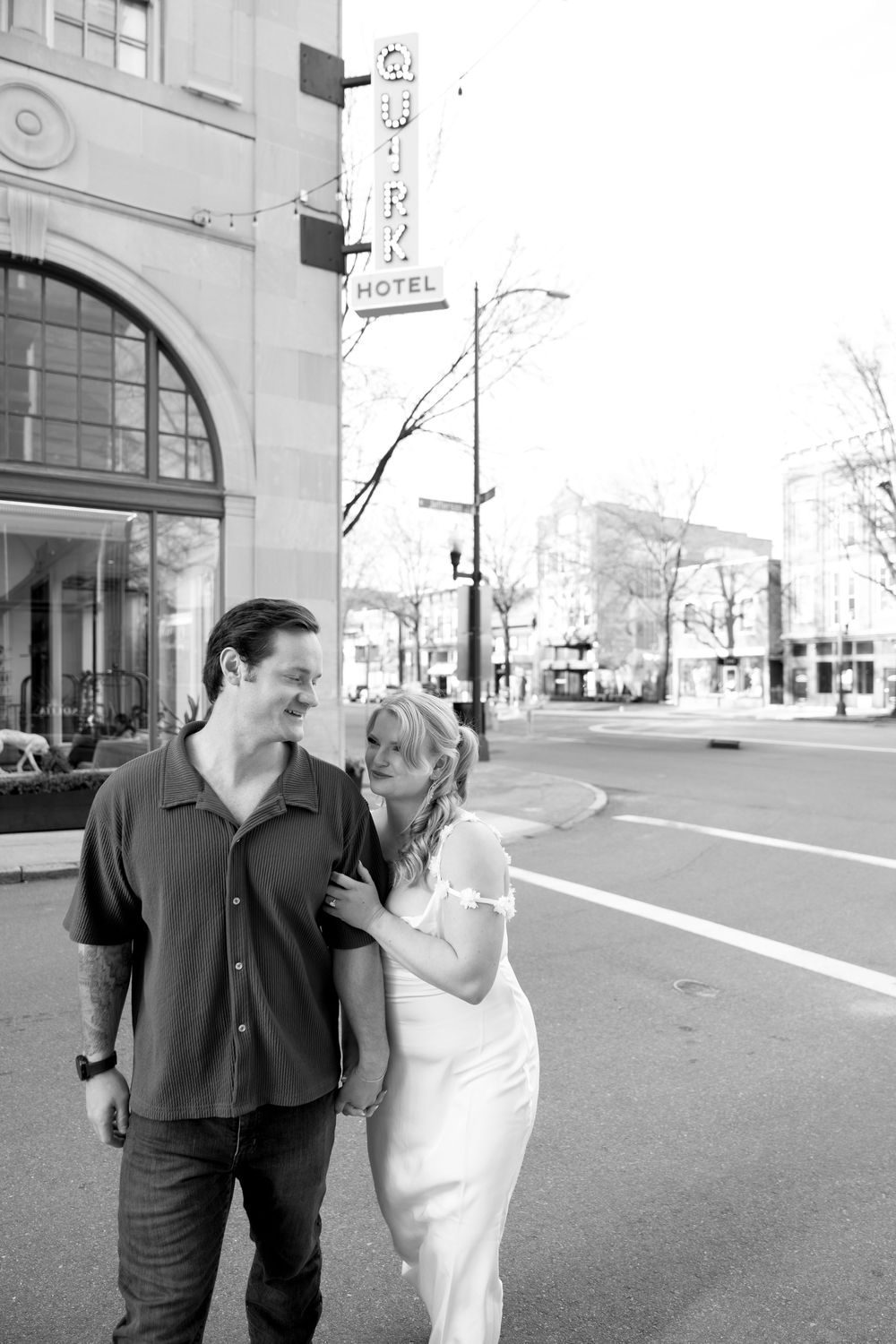 A couple strolling down a city street near vintage buildings in black and white.