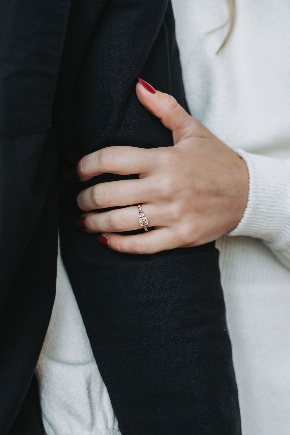 Close-up shot of a hand wearing an engagement ring against black and white clothing.