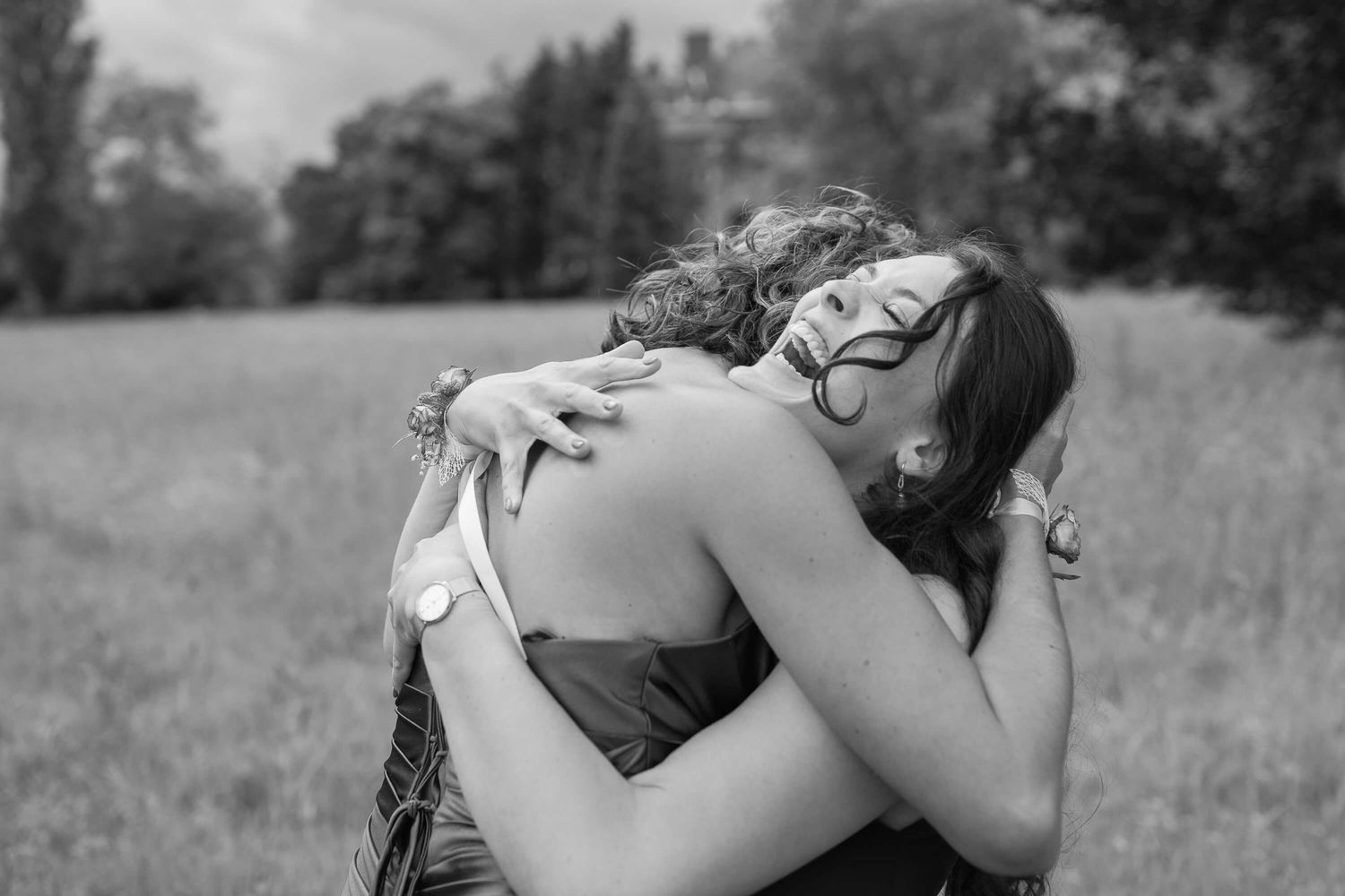 Two people embracing in an intimate hug outdoors in a grassy field with trees in the background.