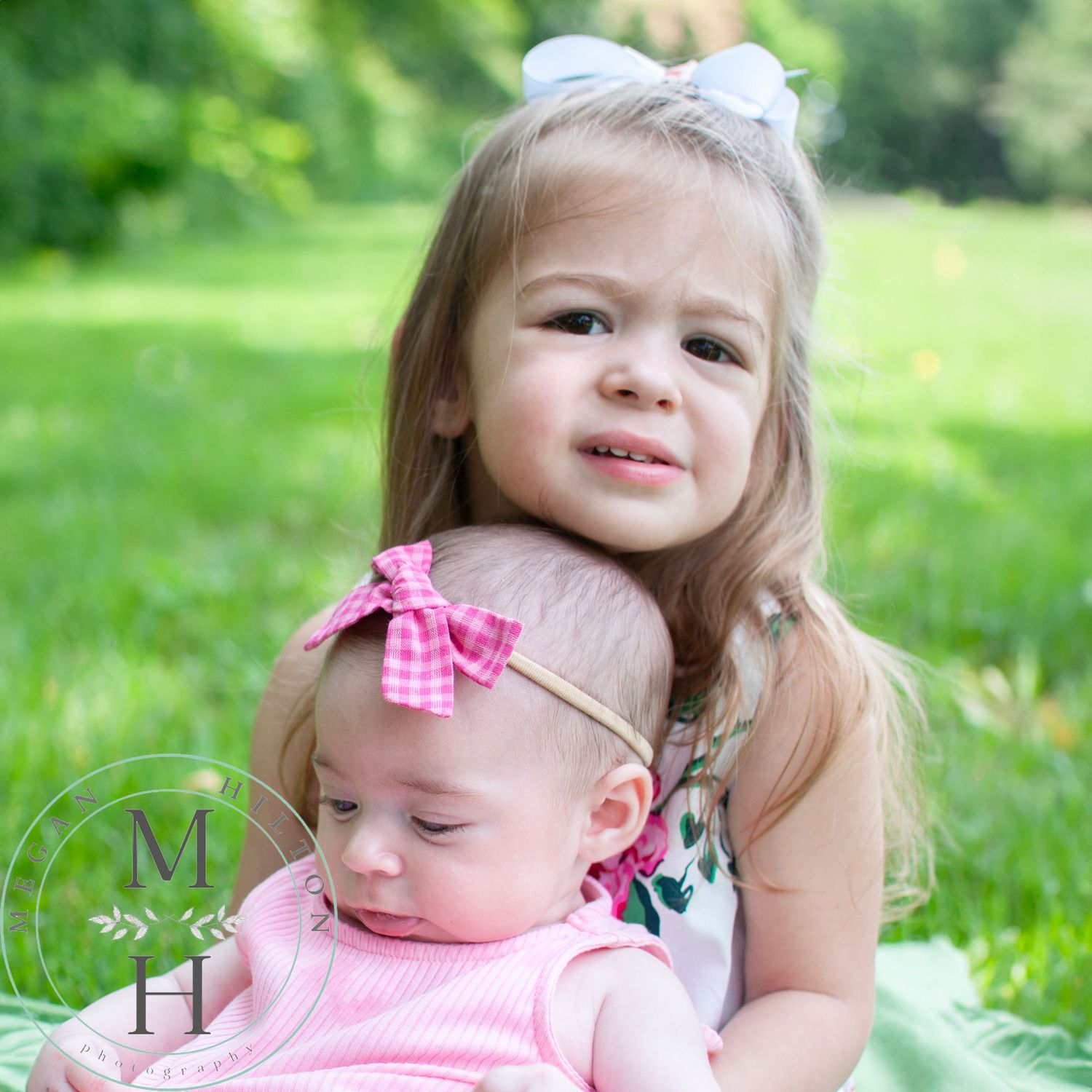 Big sister toddler holding an infant little sister outdoors.