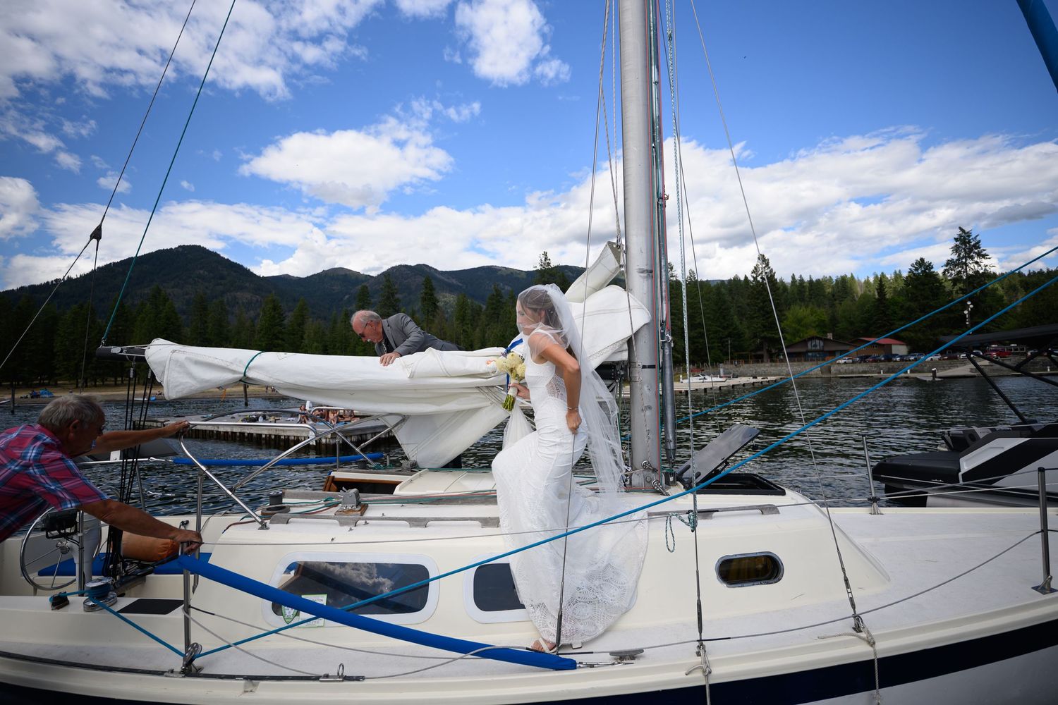 A sailboat docked at a marina on a beautiful sunny day with mountains and blue sky in the background.