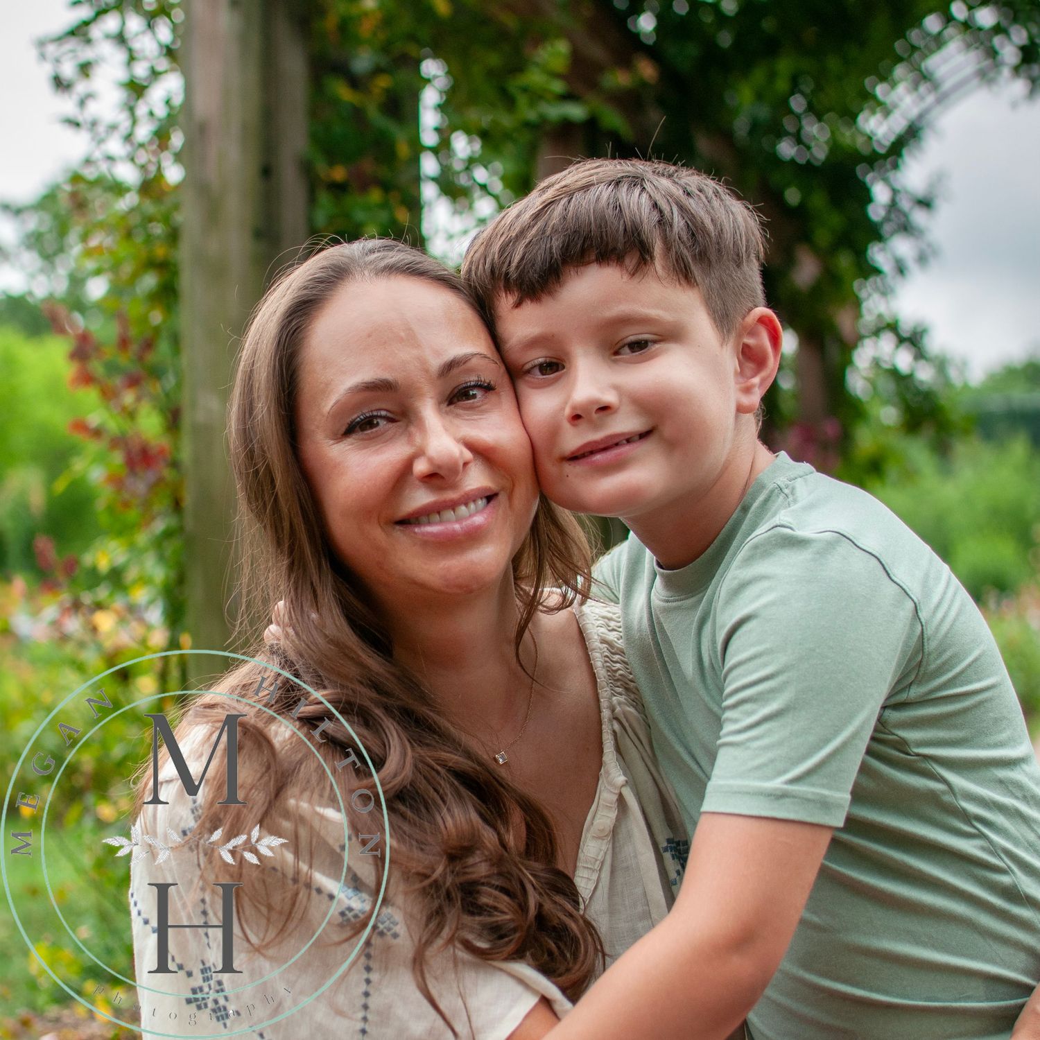A tender outdoor portrait showing affectionate embrace in a lush garden setting with vibrant flowers and greenery.