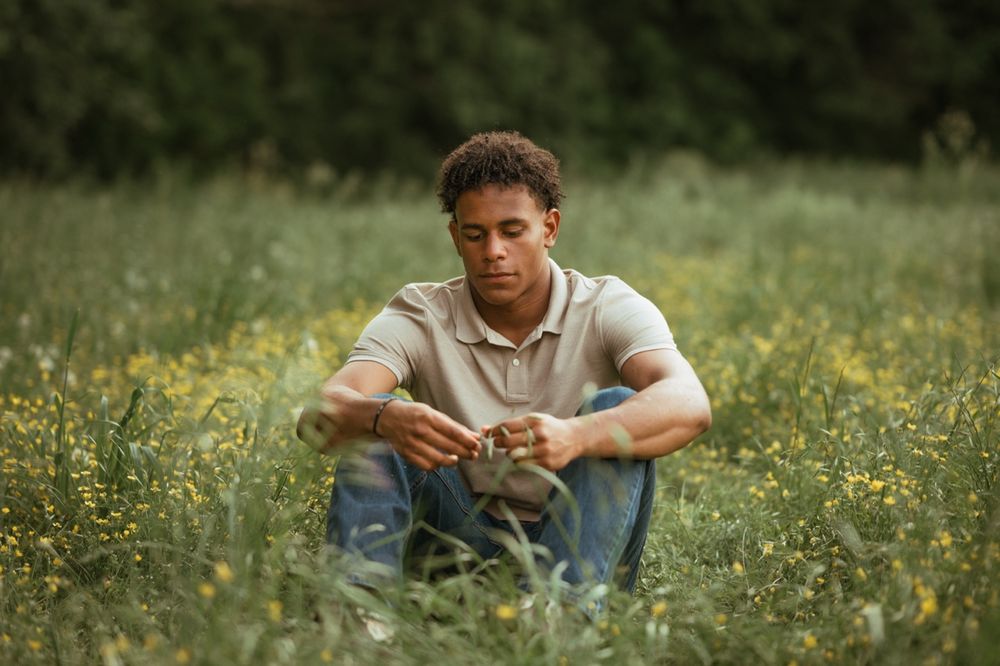 A person in casual attire relaxes in a meadow filled with yellow wildflowers on a bright sunny day.