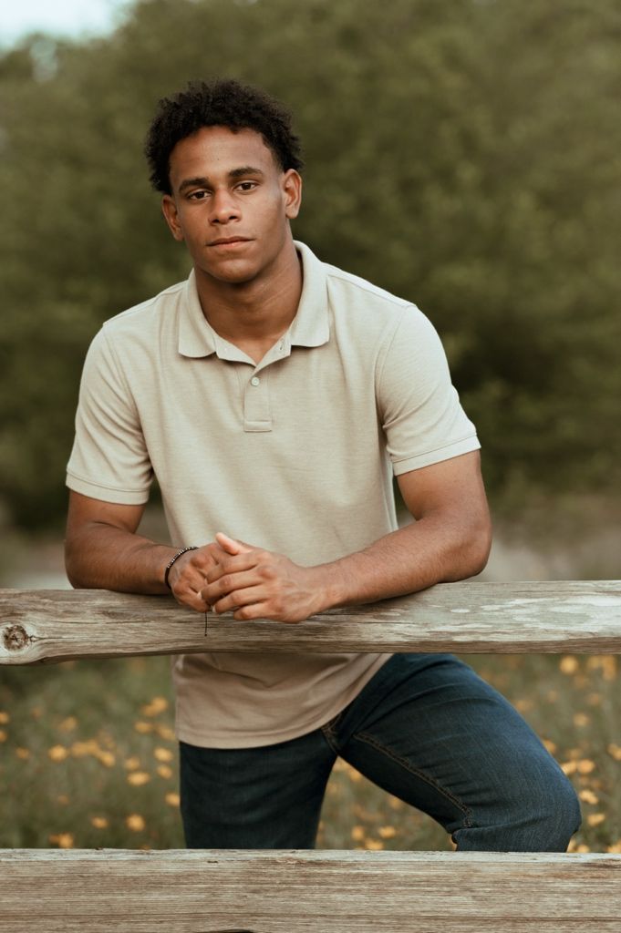 Person wearing a beige polo shirt leans against a rustic wooden surface outdoors.