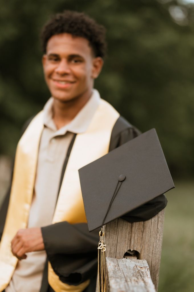 A graduate in cap and gown with golden stole holds their diploma during an outdoor graduation photoshoot.