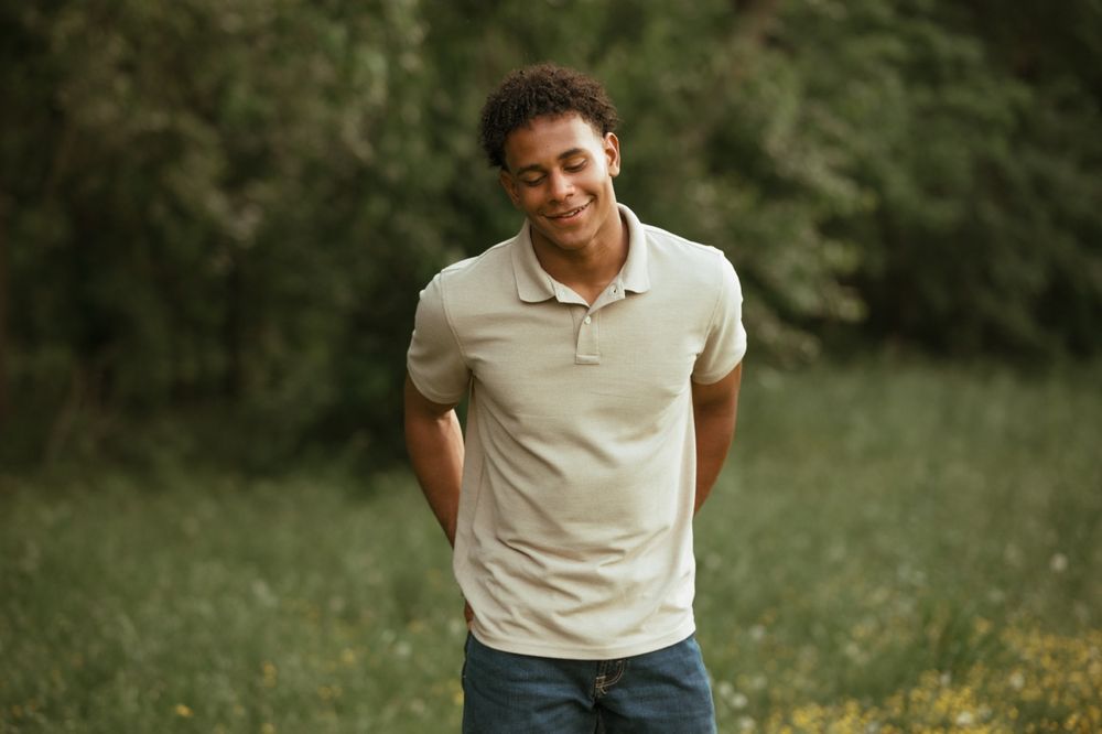 Someone wearing a cream colored polo shirt smiling outdoors in a natural setting with green foliage in background.