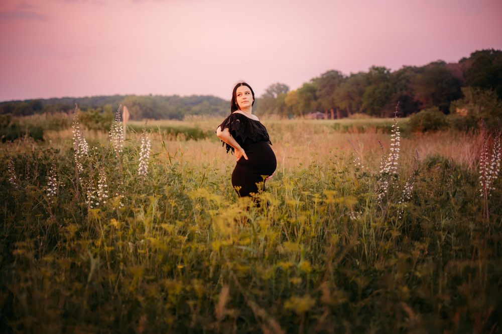 A silhouette stands in a golden wildflower meadow at sunset with tall grasses and trees in the background.
