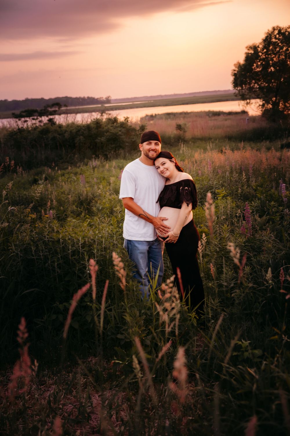 A couple embraces in a wildflower meadow at sunset with a misty lake in the background creating a romantic atmosphere.