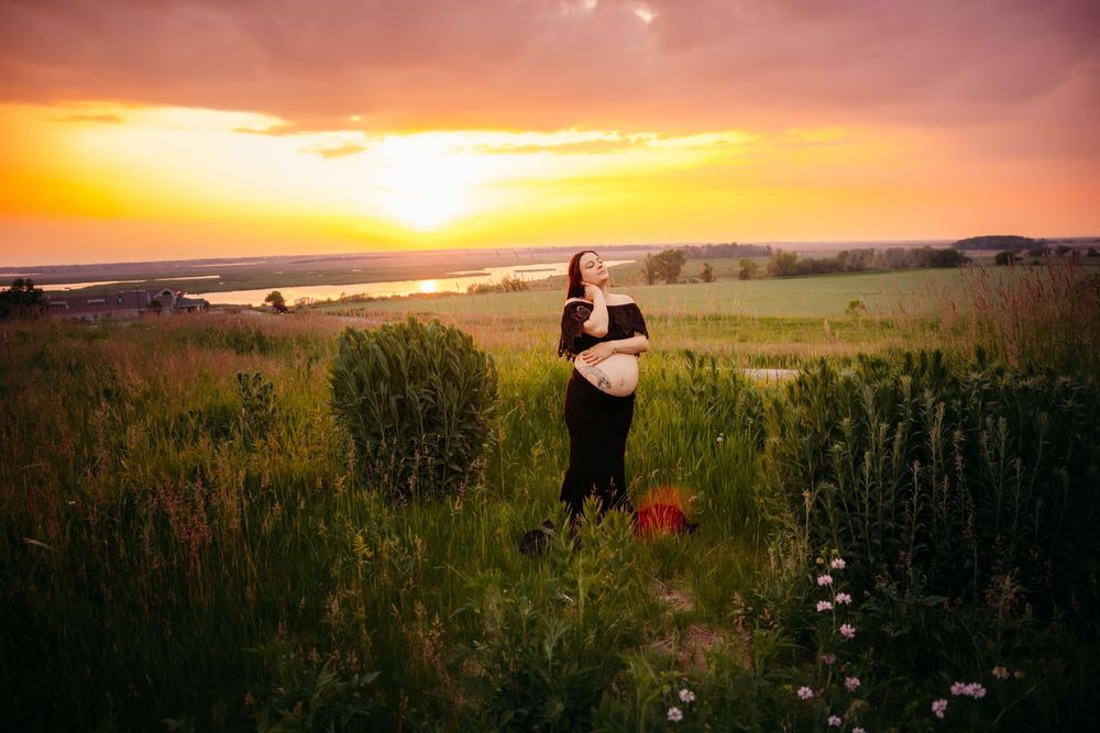 A silhouette stands in a grassy meadow at sunset with wildflowers and a golden sky in the background.