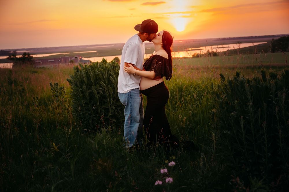 A couple embraces in a field during a golden sunset as the warm light illuminates their silhouettes against the horizon.