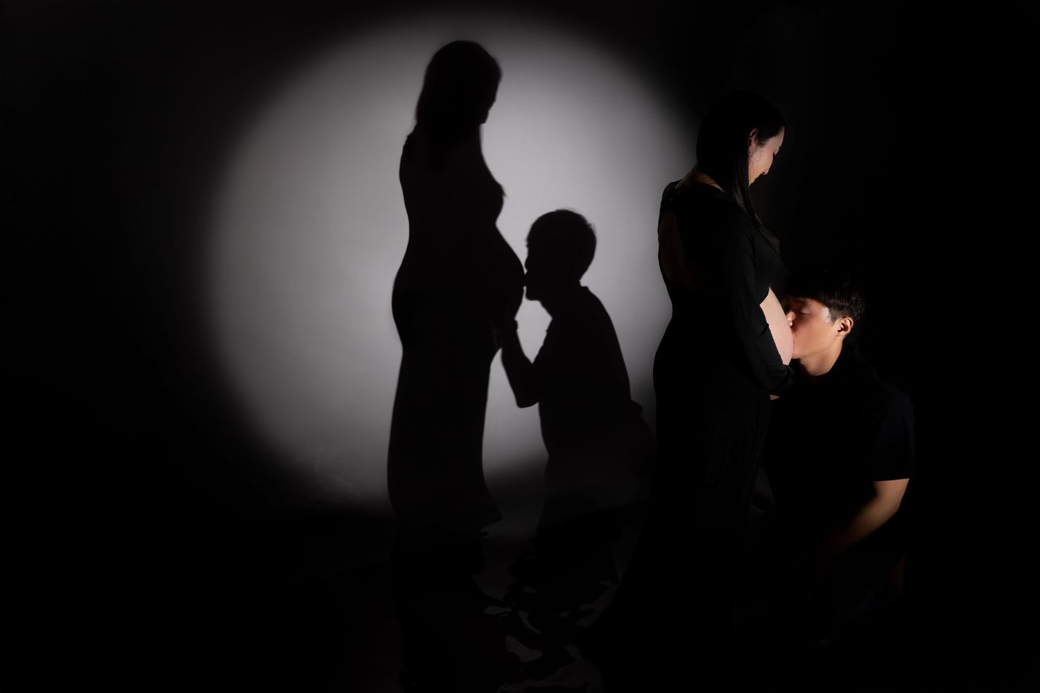 Silhouettes of people cast dramatic shadows against a white spotlight on dark background.