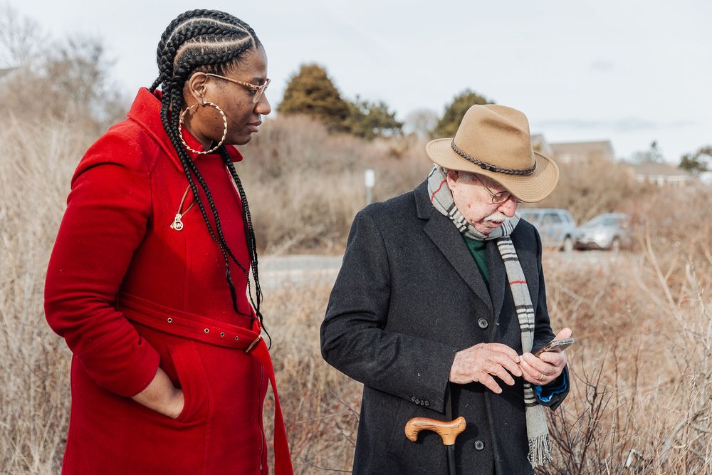 Two people outdoors, one wearing a red coat and the other in dark clothing looking at a mobile phone.