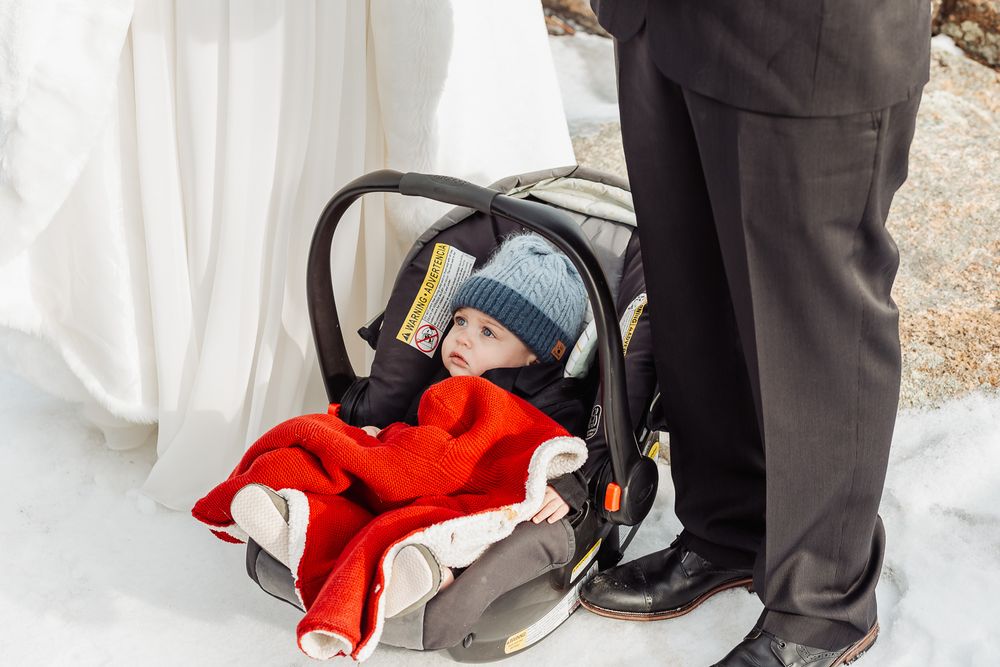 Baby bundled in red blanket sleeping peacefully in car seat during winter wedding ceremony.