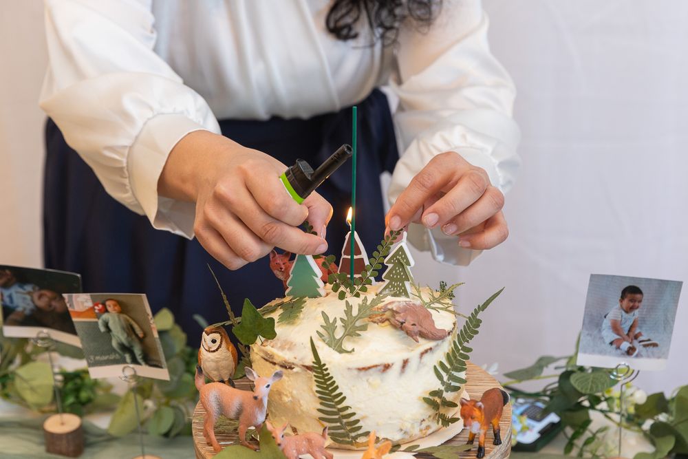 Close up shot of hands decorating a cake with greenery and floral elements on a table with scattered botanicals.