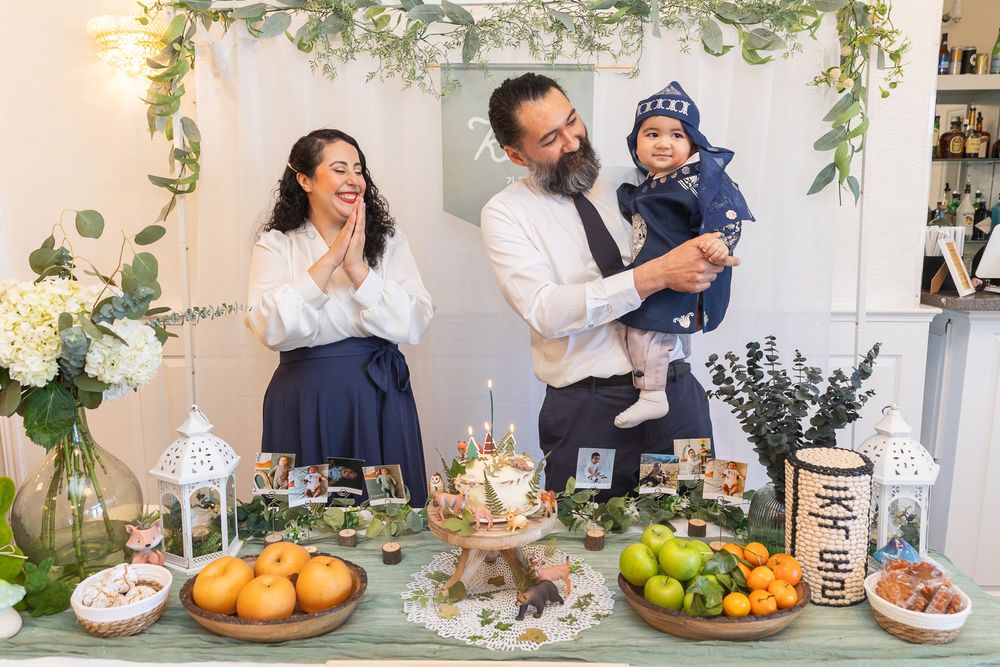 A celebratory scene with a decorated table full of fruits and desserts under a floral arch.