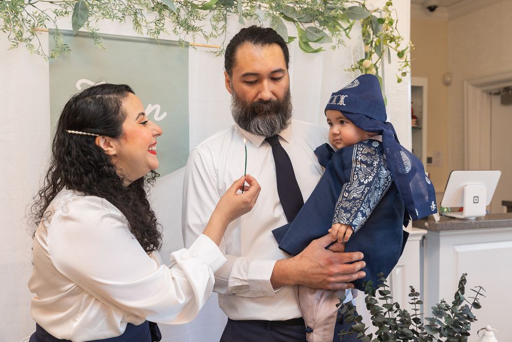 A family enjoys a playful moment together in front of a white wall decorated with greenery.