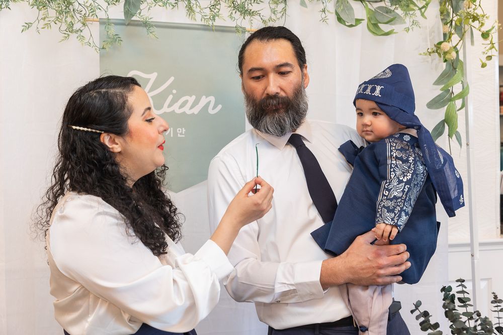 Three people share a joyful moment in front of a white wall with greenery decor.