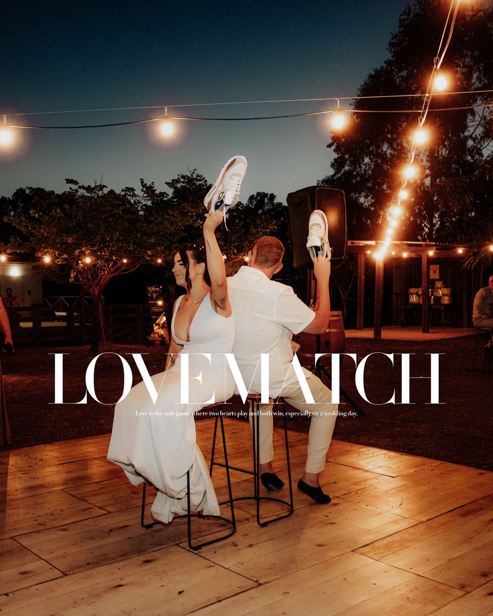 A couple plays a shoe game at their wedding reception under string lights on a wooden deck.
