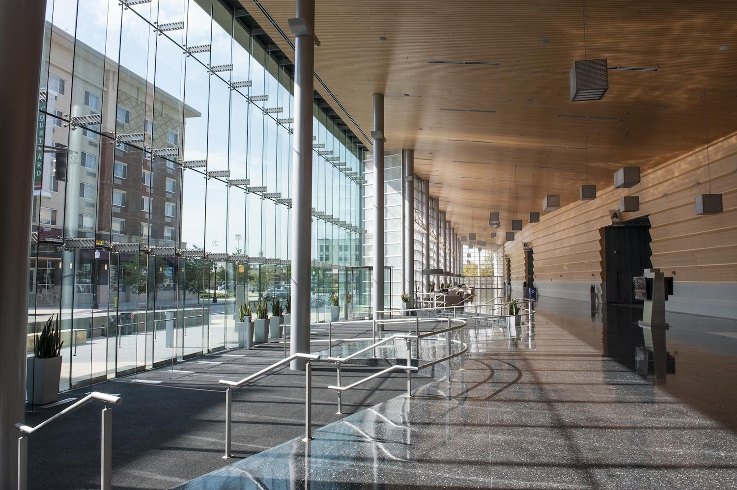 Modern architectural corridor with glass walls, wooden ceiling, and metal railings in a contemporary building interior.