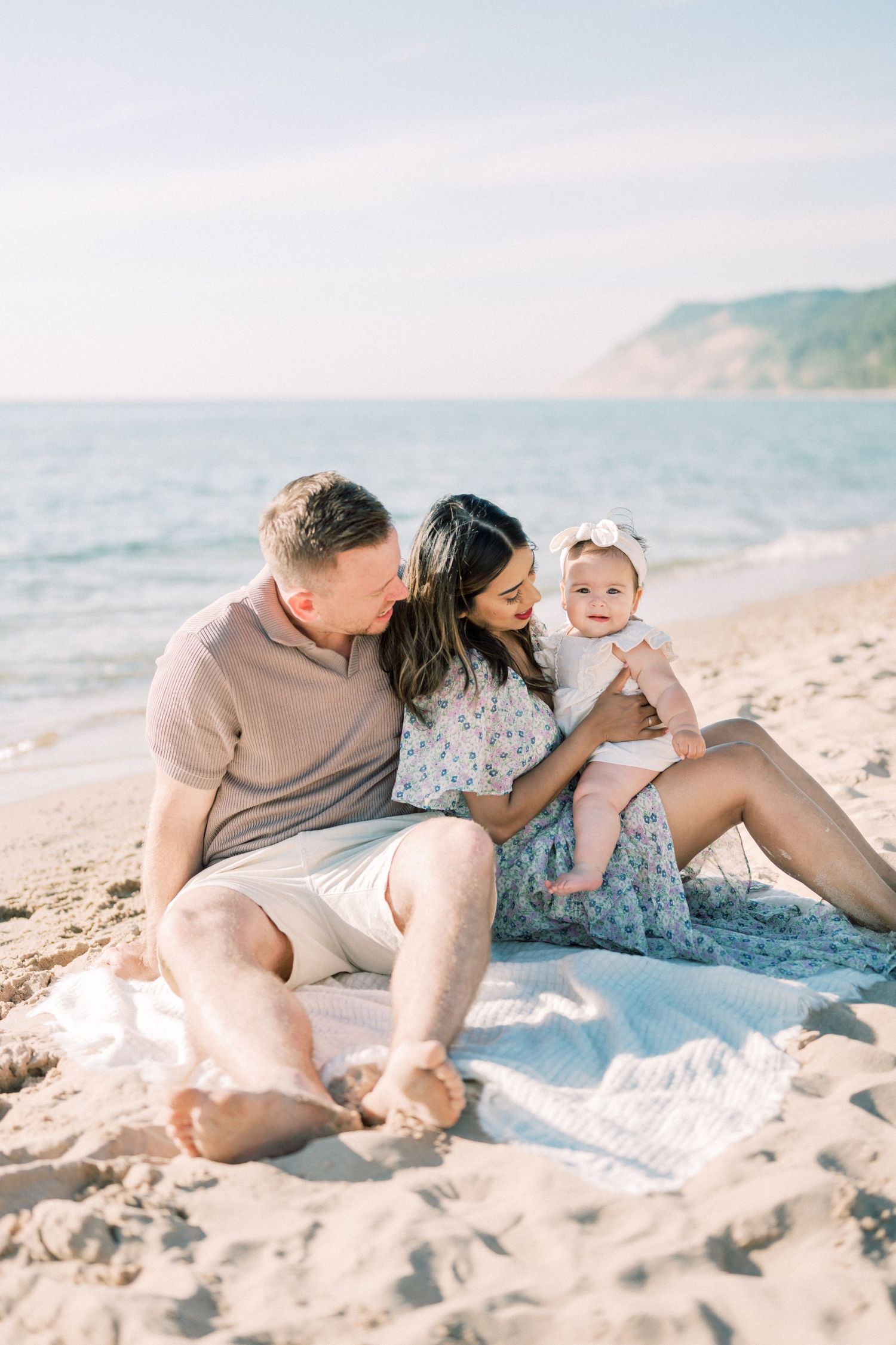 Family relaxing together on blanket at scenic beach with cliffs in background.