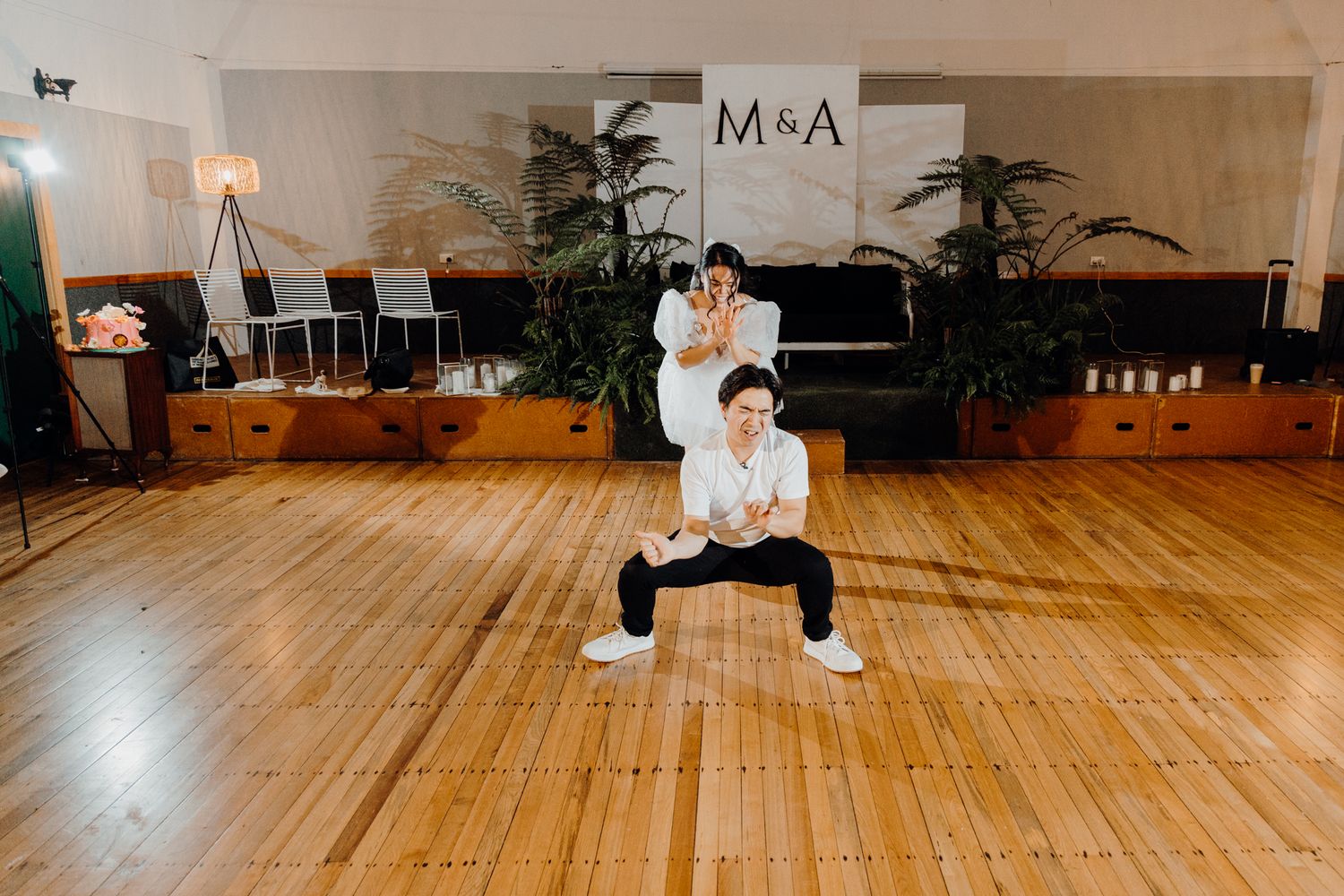 Modern indoor photo session against white wall with M&A letters and plants in background.