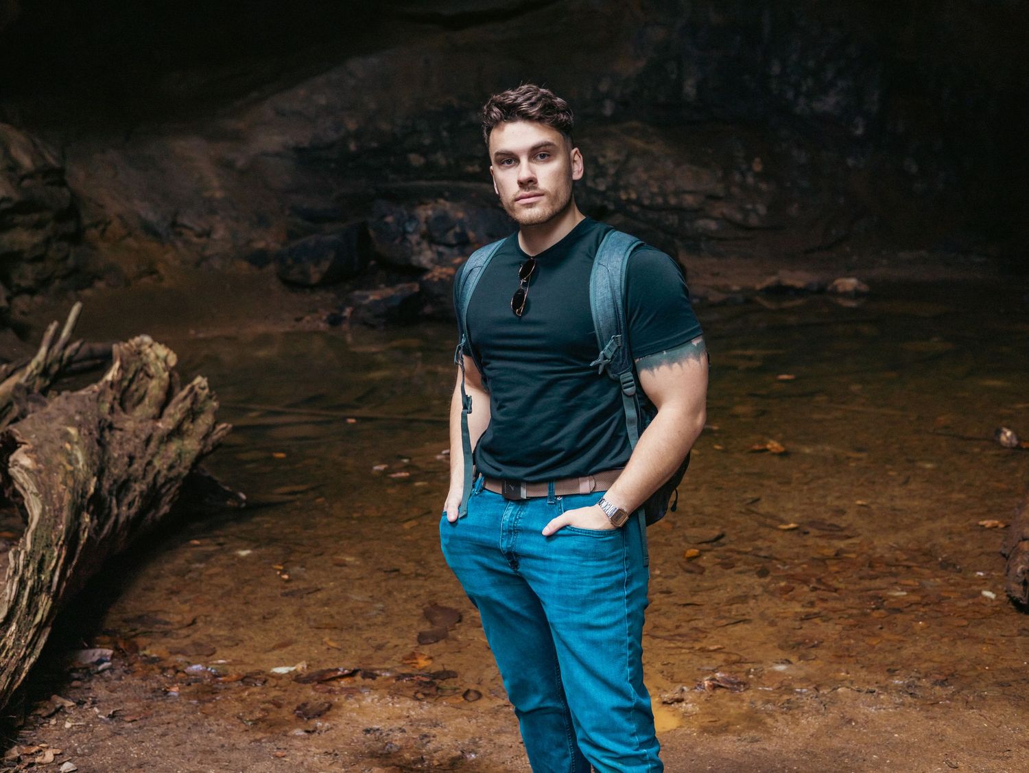 Person posing casually against a rocky cave wall background.