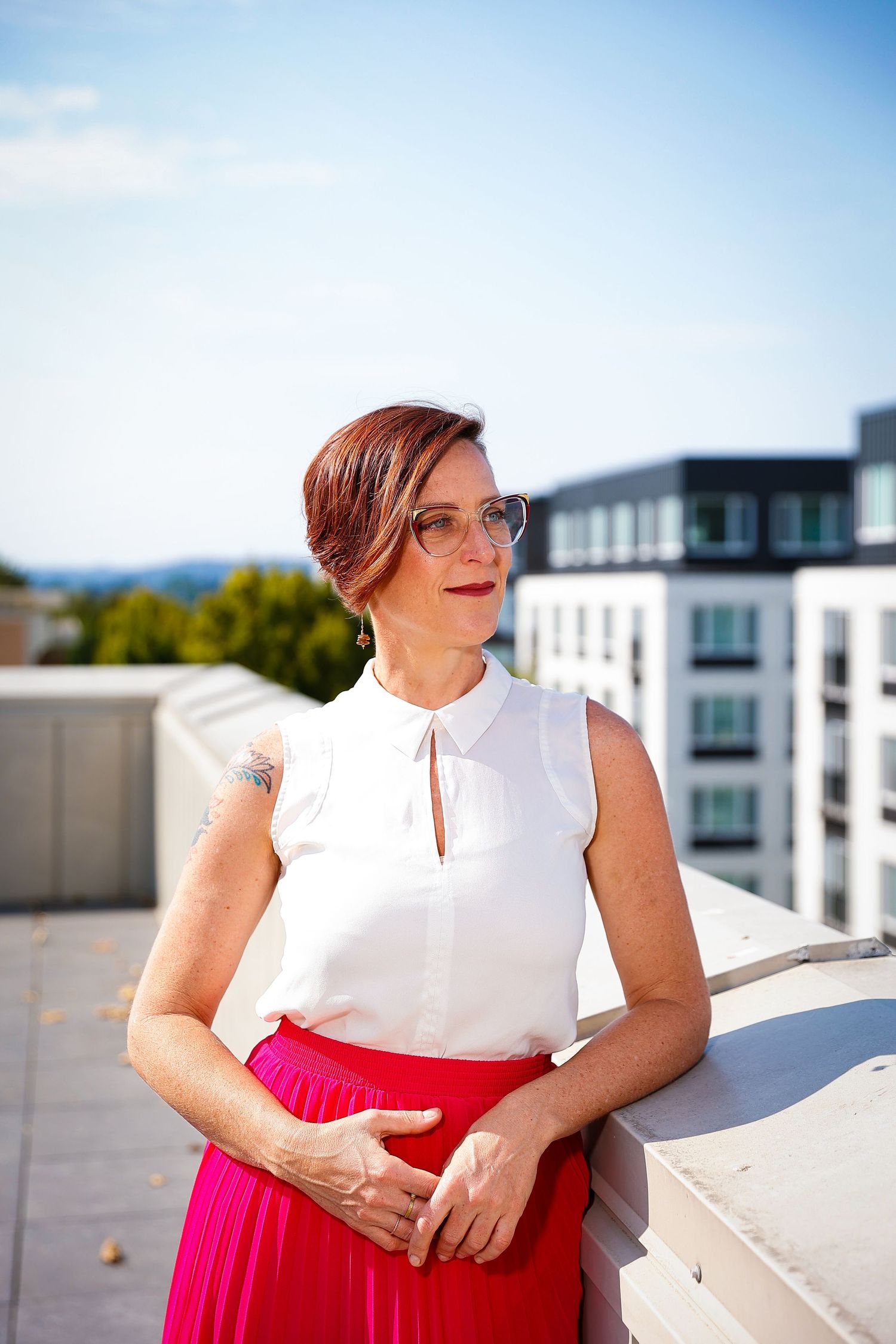 Professional portrait on urban rooftop with modern buildings and blue sky in background.