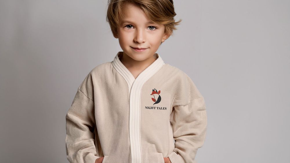 Child wearing a cozy cream-colored sweater with embroidered details stands against a neutral background.