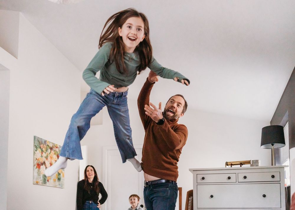 A joyful indoor scene of people jumping and playing together in a bright white room.