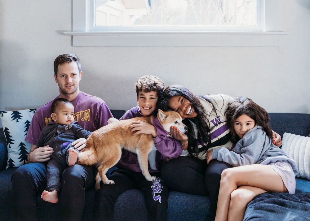 Family relaxing together on grey couch with their dog in bright living room.