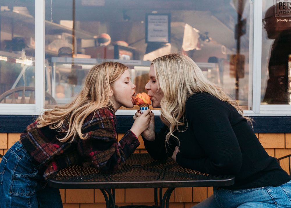 Two friends share a croissant while sitting at an outdoor cafe counter.